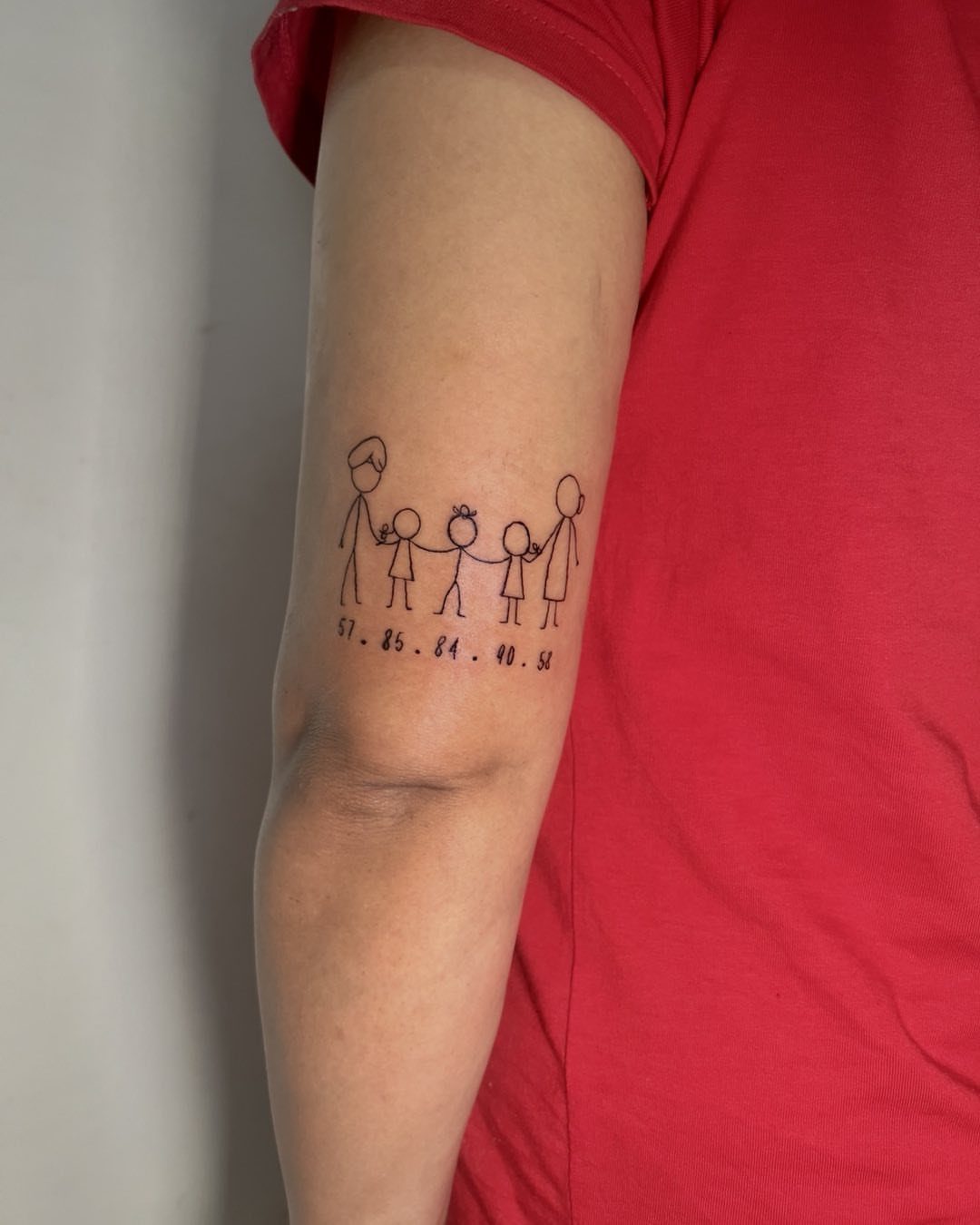 Stick figure family tattoo on an arm with dates written underneath in black ink.
