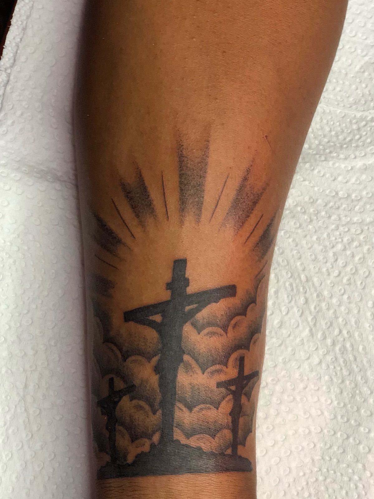 Crucifixion tattoo on an arm featuring Jesus on a cross with clouds and rays.