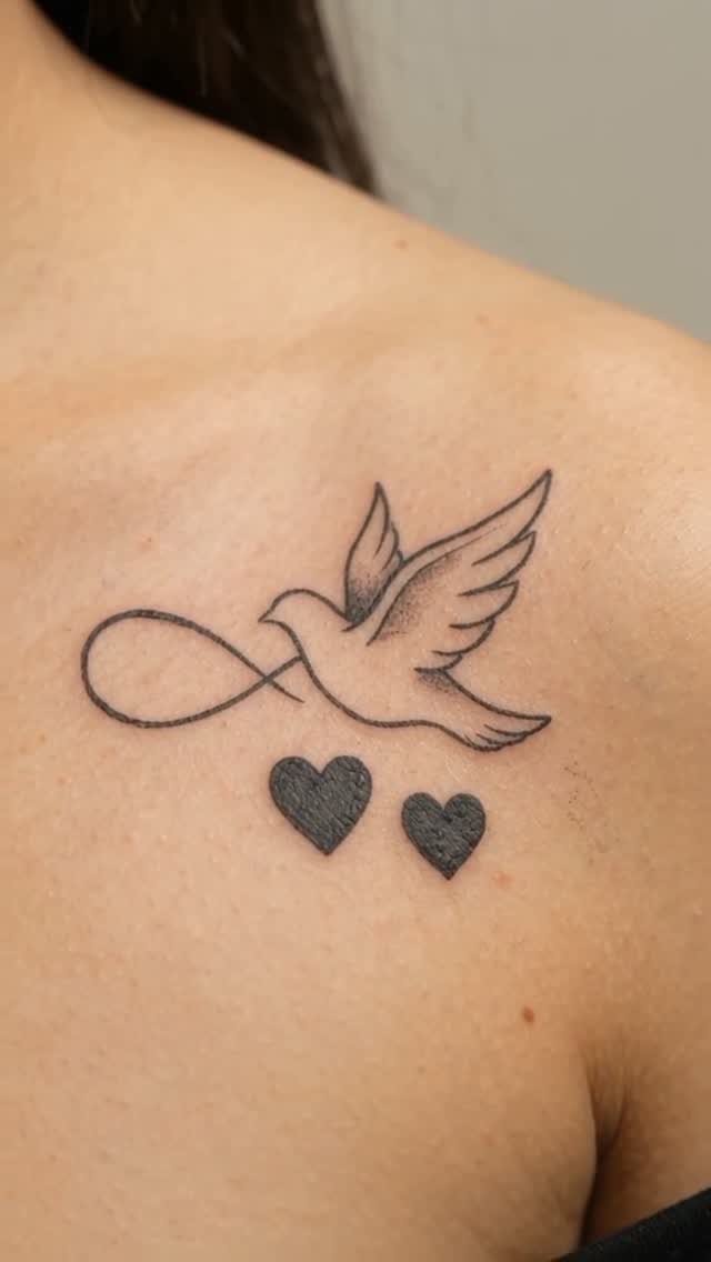 Dove tattoo with an infinity symbol and two small hearts on a shoulder.