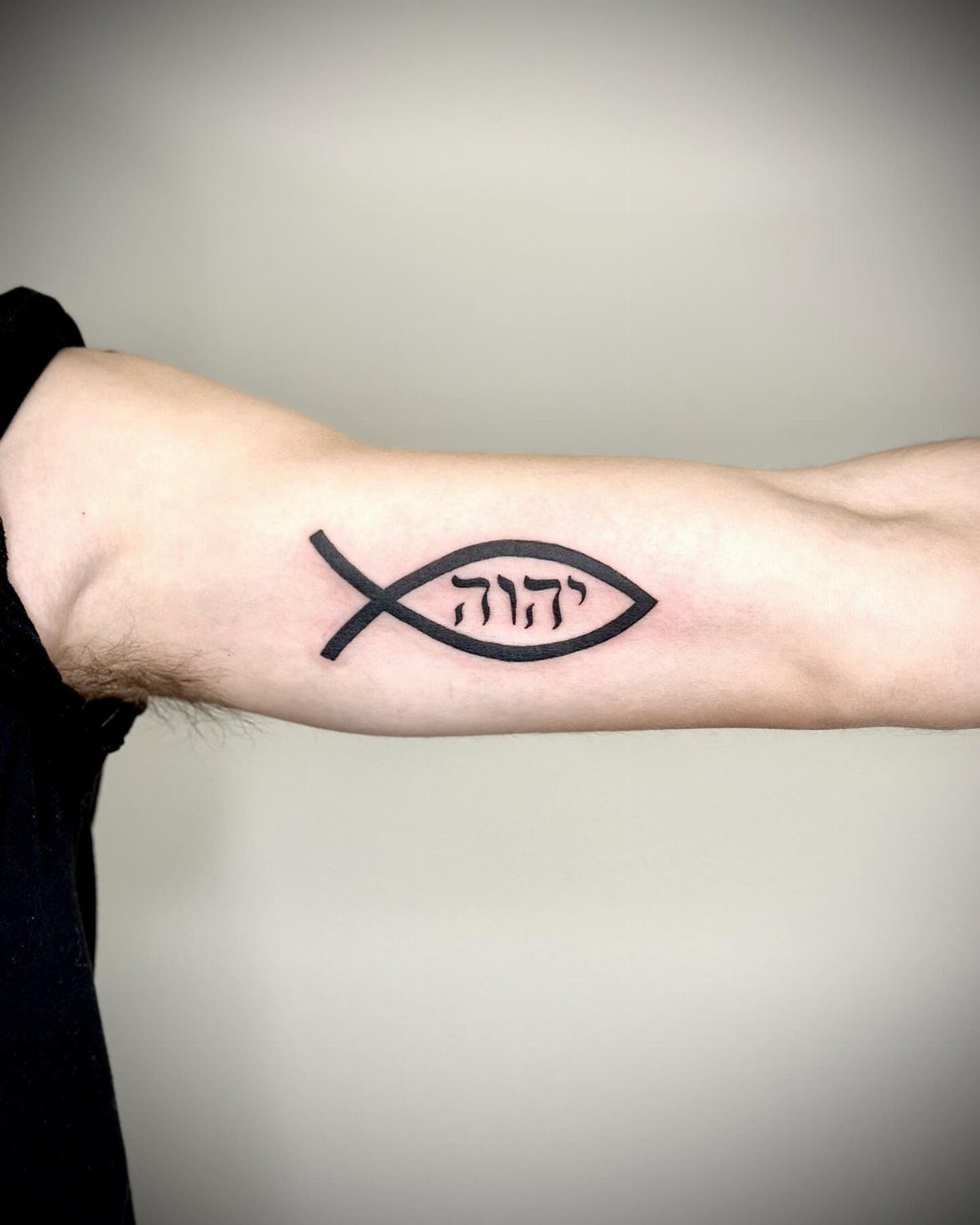 Ichthys fish symbol tattoo with Hebrew lettering on a person's forearm.