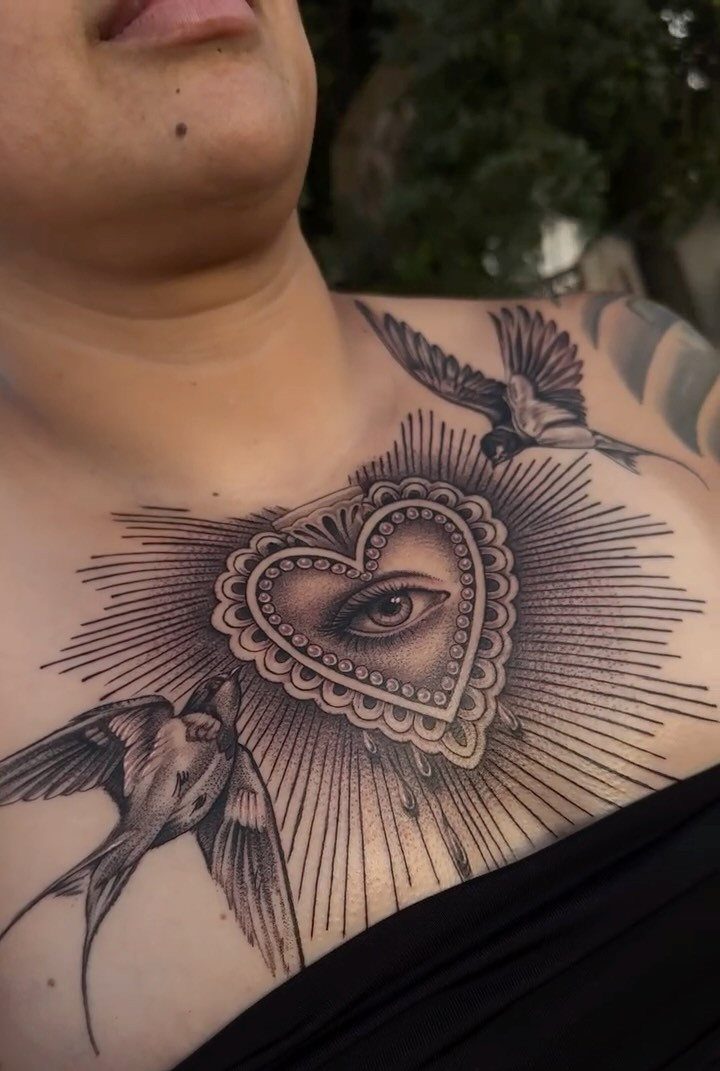 Heart tattoo with an eye in the center and two swallows on a chest