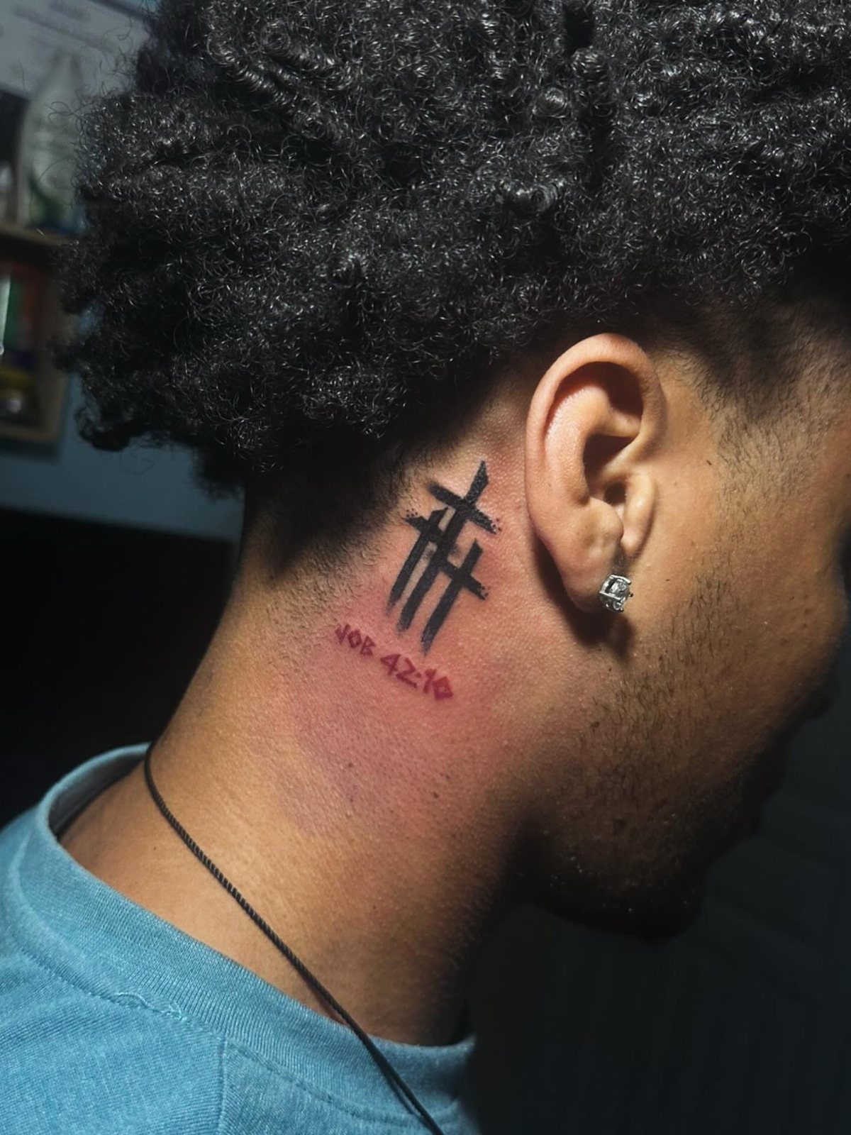 Small cross tattoo with red scripture text on a person's neck
