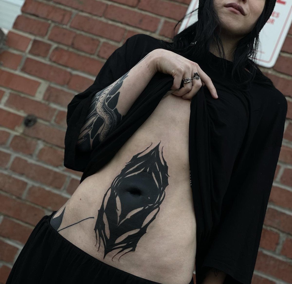 Tattoos Around Belly Button: 8 Best Ideas to Consider 8 Abstract black ink tattoo surrounding the belly button of a person against brick wall