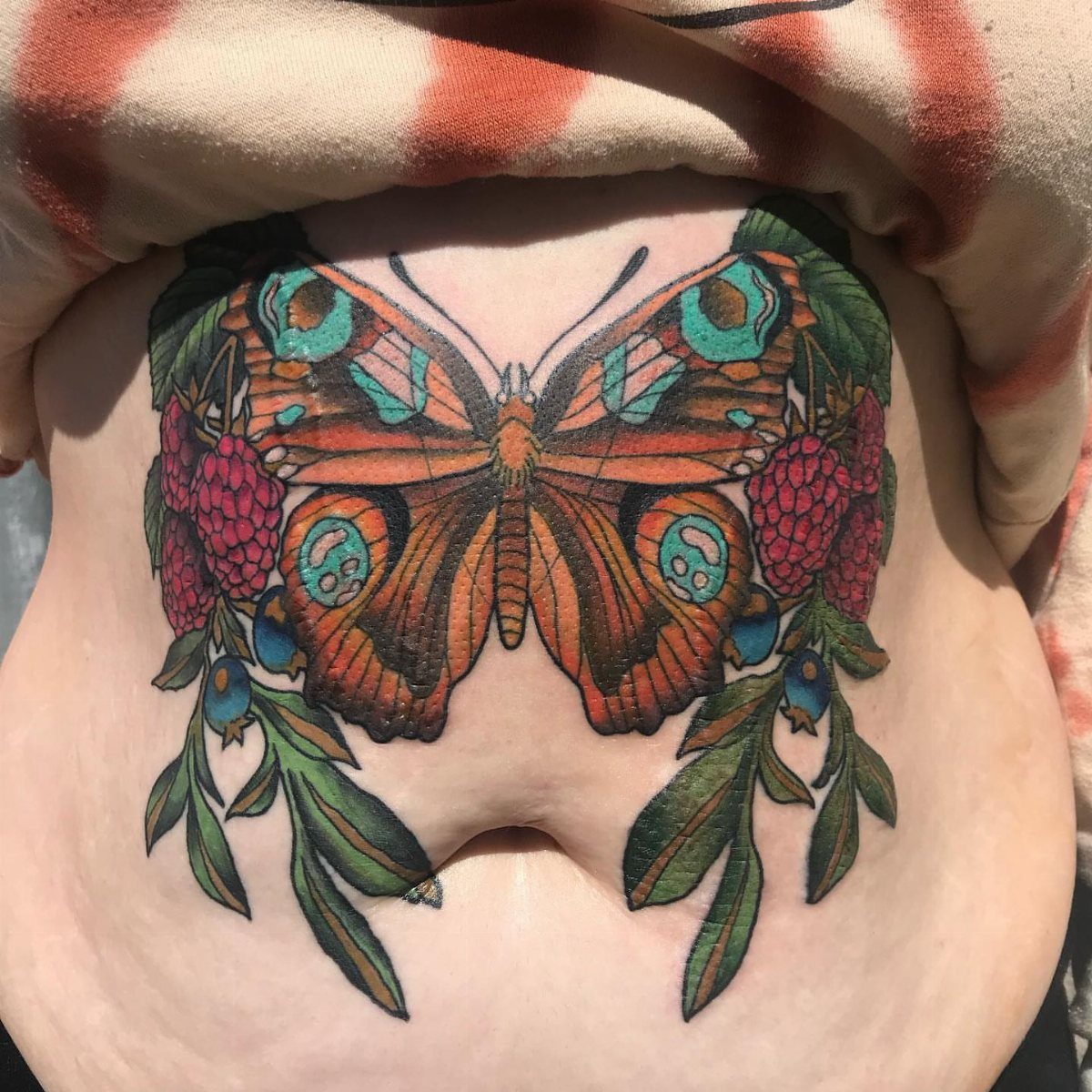 Tattoos Around Belly Button: 8 Best Ideas to Consider 5 Butterfly tattoo with berries and leaves on a person's stomach above the navel.