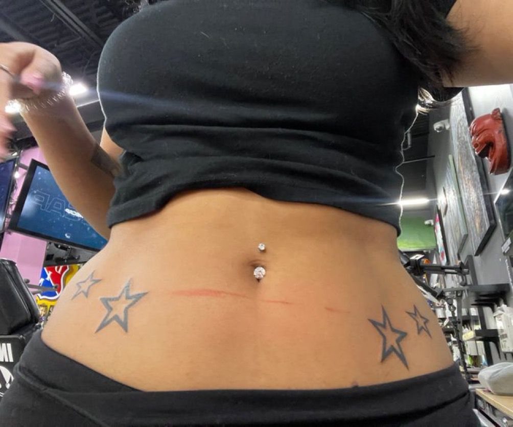 Tattoos Around Belly Button: 8 Best Ideas to Consider 3 Star tattoos on the sides of a belly button with a silver piercing