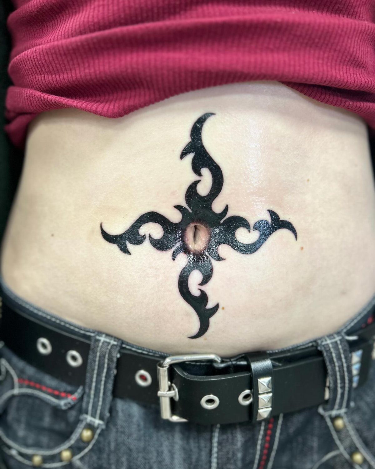 Tattoos Around Belly Button: 8 Best Ideas to Consider 4 Black tribal tattoo with symmetrical curved shapes centered around a person's belly button.