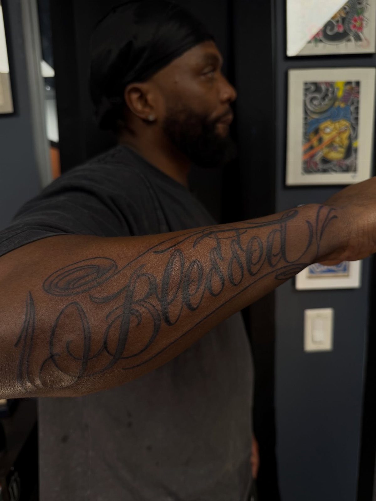 Bold black script tattoo reading Blessed on a Black man's forearm