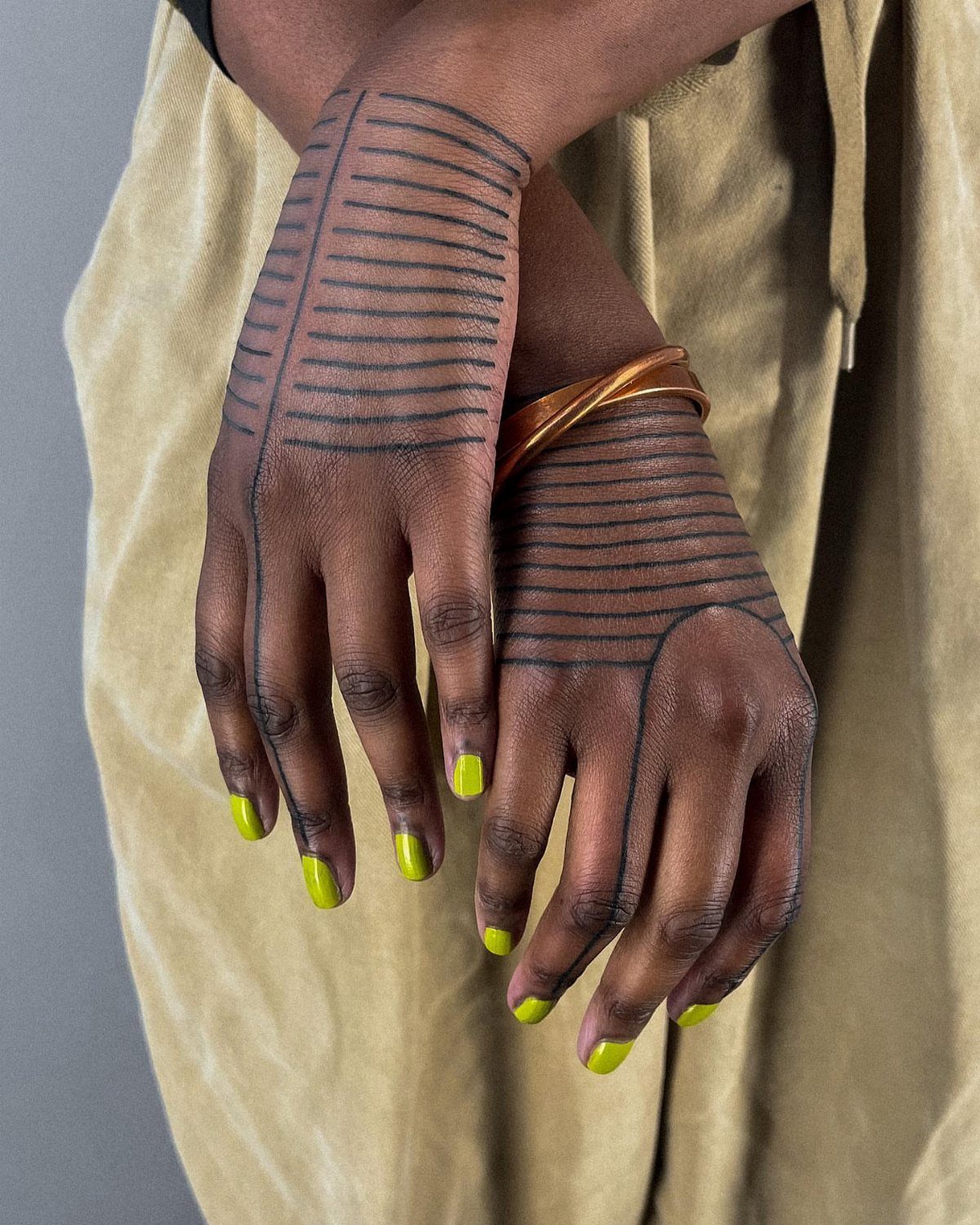 Hands with dark skin featuring black line tattoos and bright yellow nail polish.