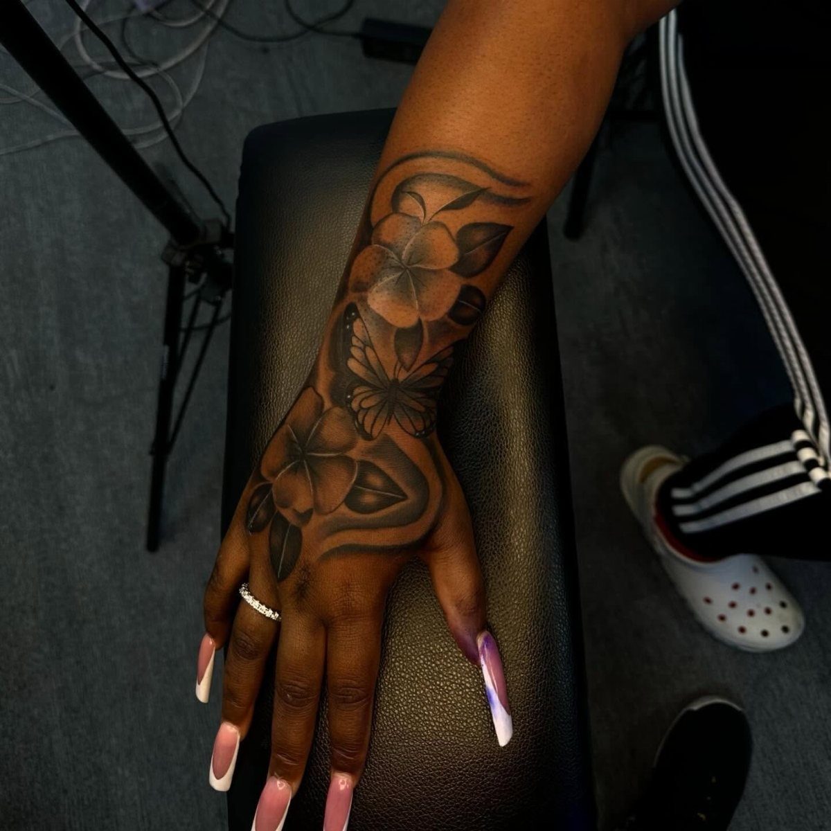 Floral and butterfly tattoo on the hand and forearm of a person with dark skin