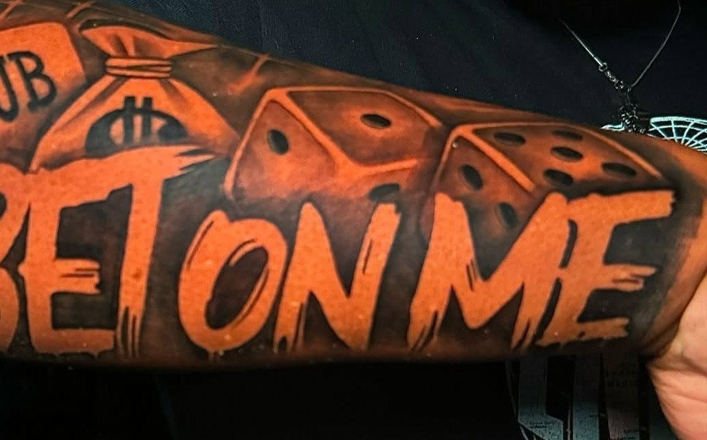Tattoo on dark skin with orange dice and text saying BET ON ME