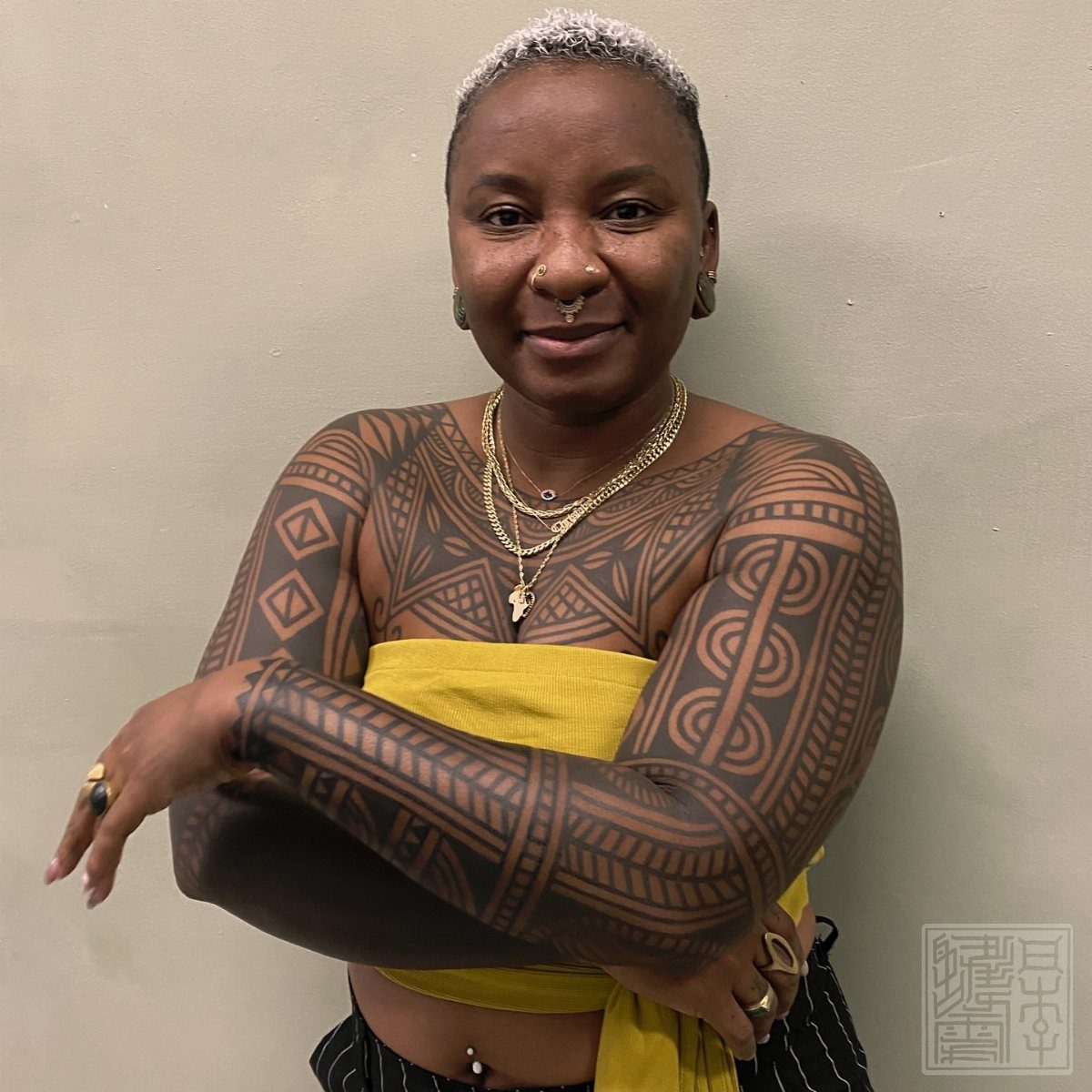 Black woman with intricate tribal and geometric black ink tattoos on her arms and chest