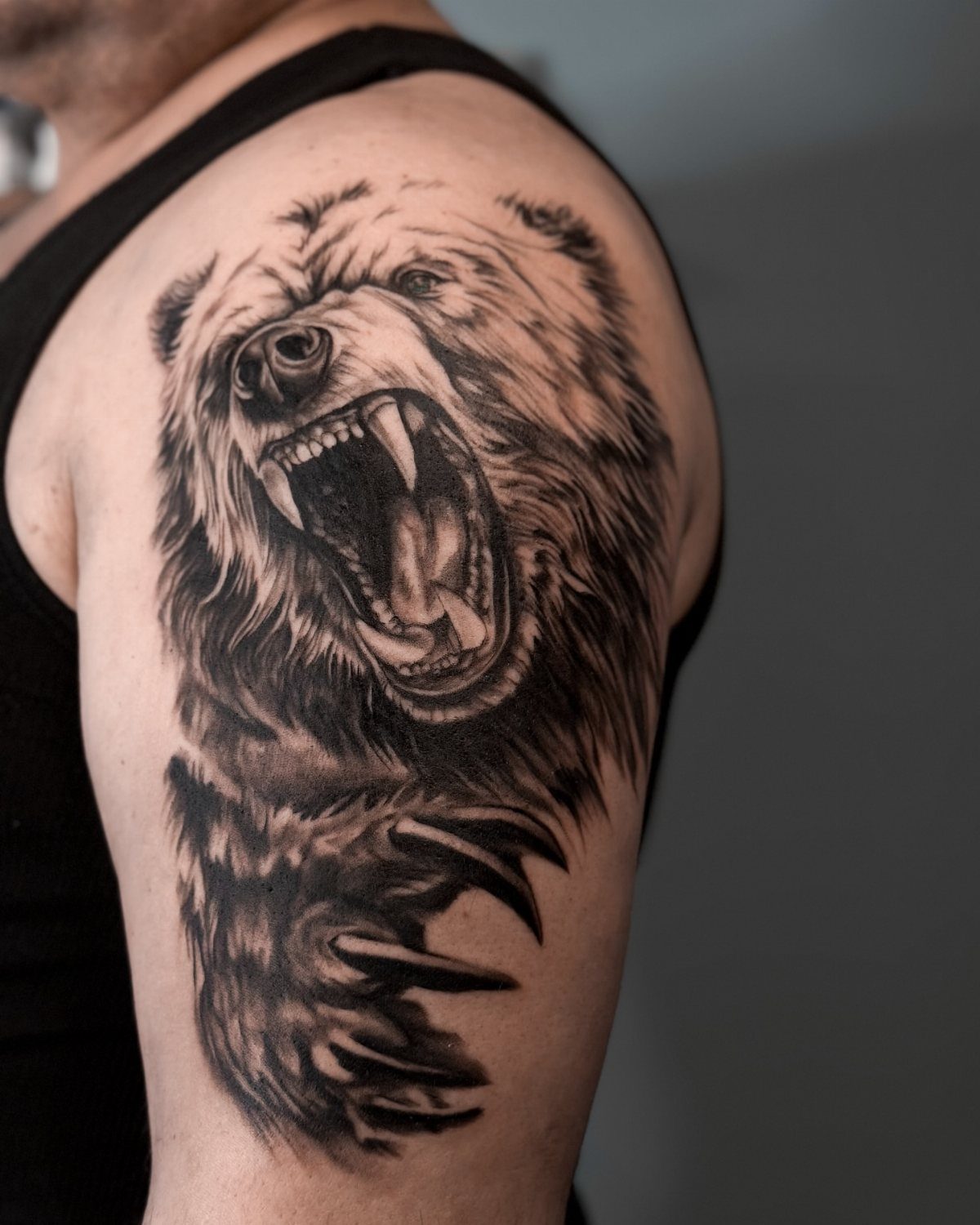 Bear claw and roaring bear head tattoo on a man's upper arm.