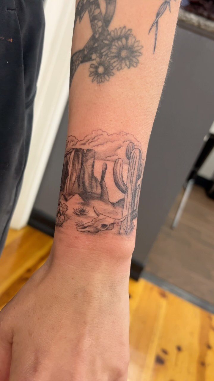 Desert scene tattoo on forearm featuring a saguaro cactus and animal skull.