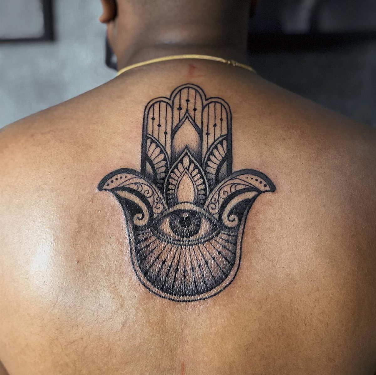 Hamsa hand tattoo with an eye centered on a person's upper back.