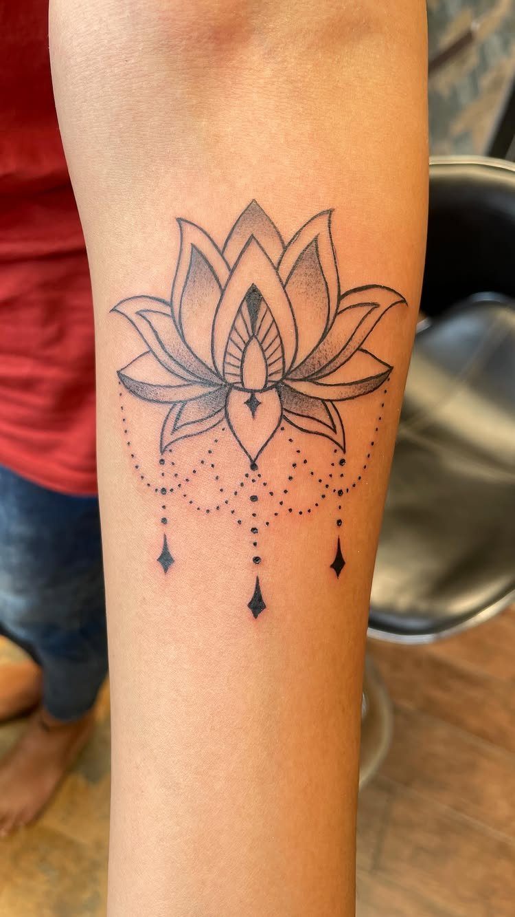 Lotus flower tattoo with decorative dot work on a person's forearm.