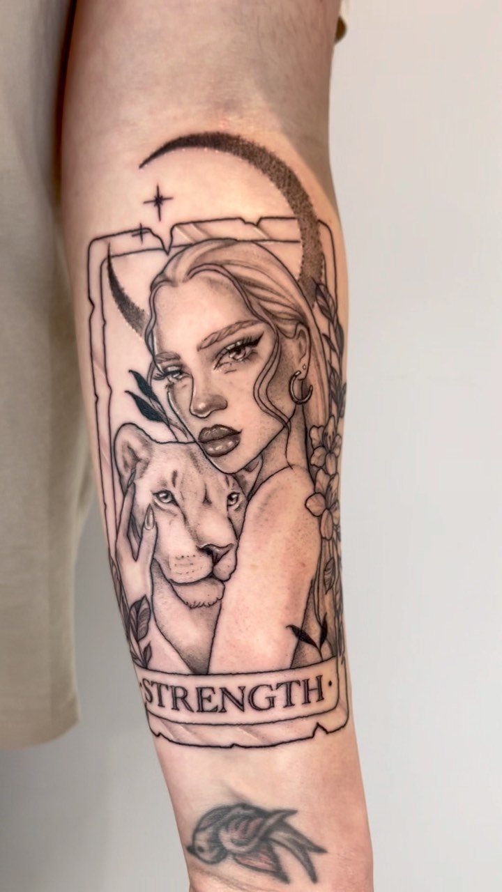 Strength tarot card tattoo on forearm featuring a woman and a lion