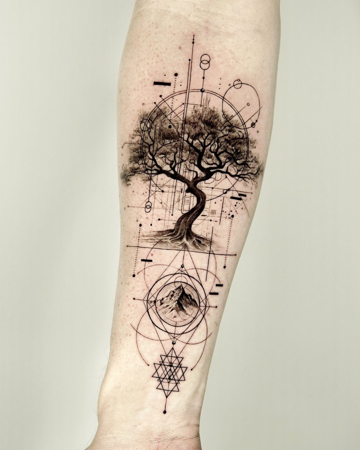 Tree tattoo with geometric shapes and a mountain on a person's forearm