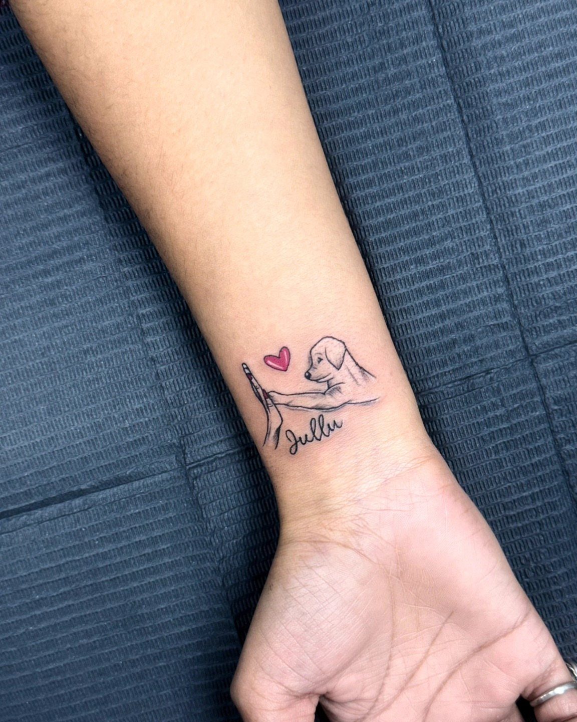 Wrist tattoo of a dog and hand with a pink heart and name.