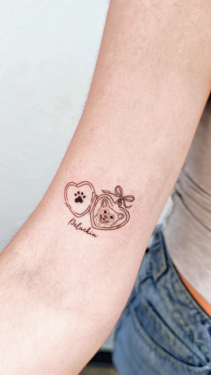 Heart locket tattoo on forearm containing a dog portrait and a paw print