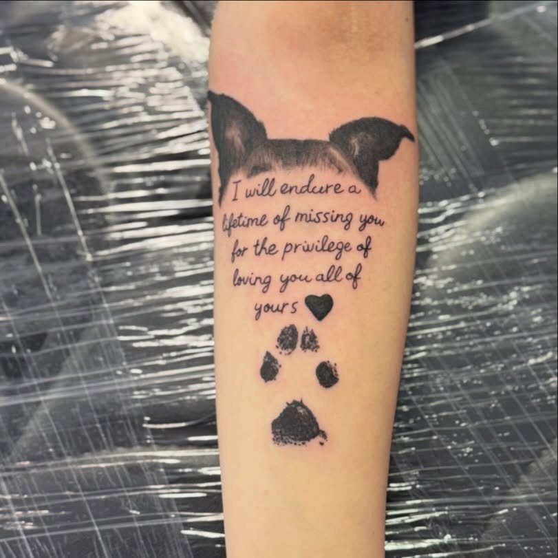 Forearm tattoo with a dog silhouette, memorial quote, heart, and paw print.