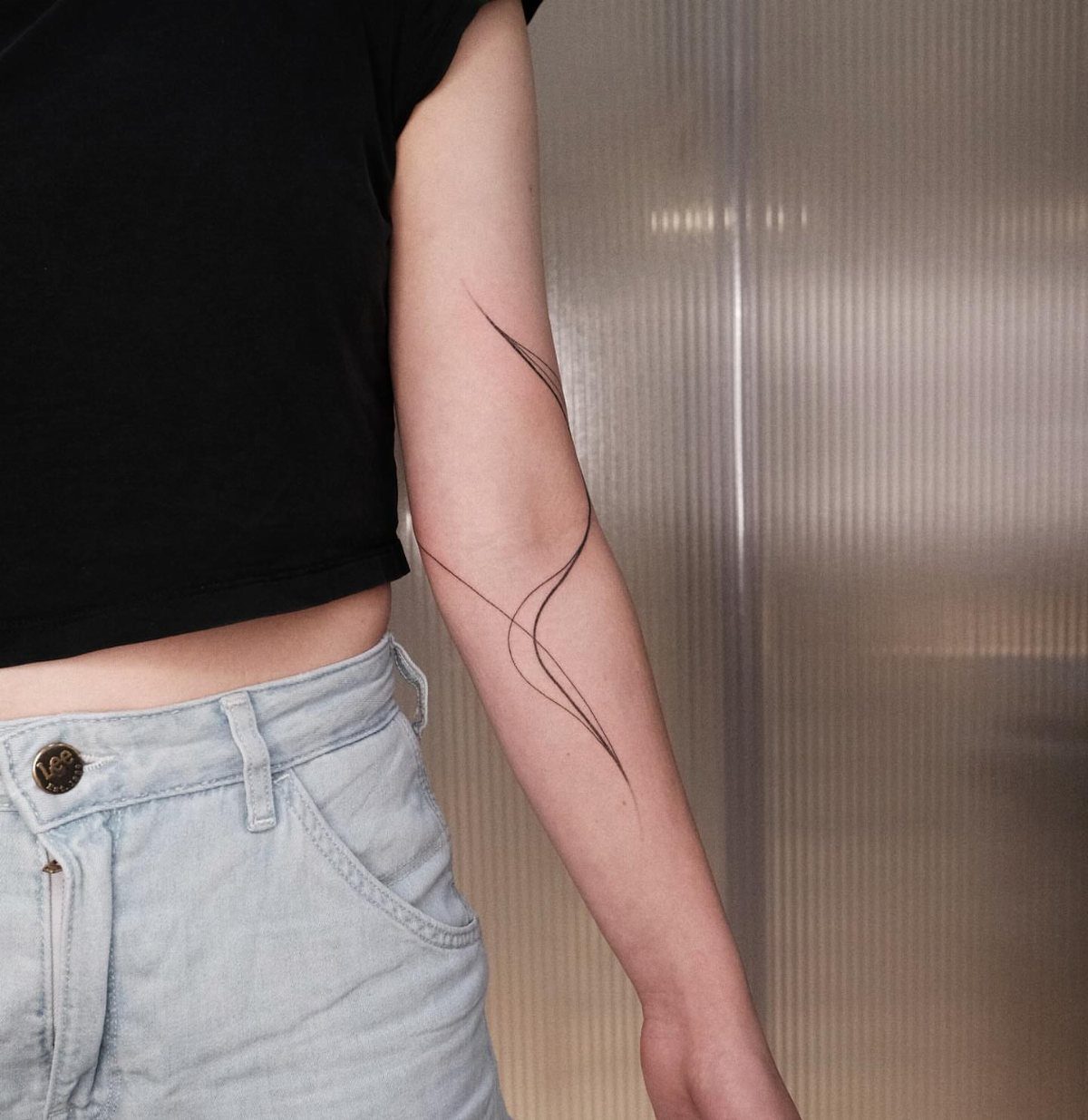 Forearm with thin dark swirling lines drawn on the skin as a tattoo.