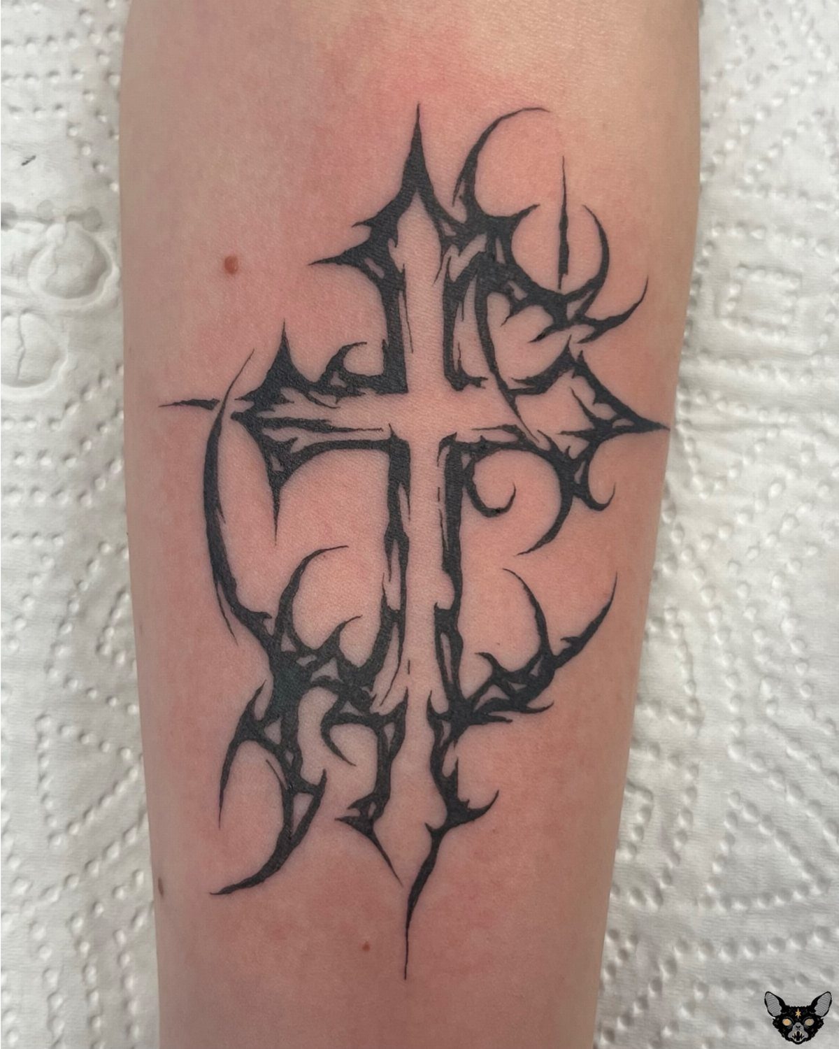 Stylized cross tattoo with sharp curved edges on a person's forearm