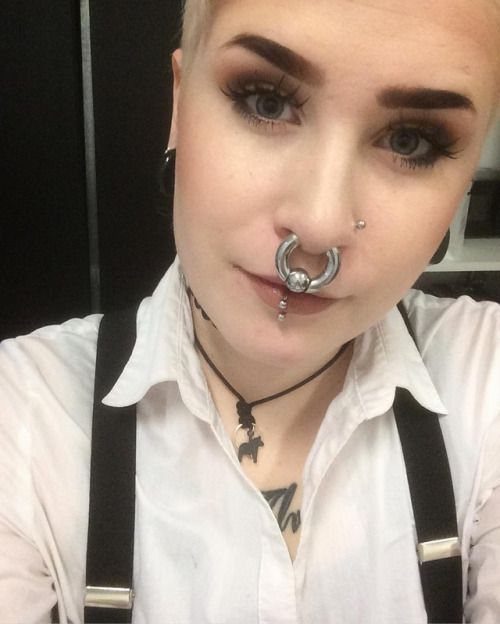Person with a thick silver circular barbell septum piercing and white collared shirt