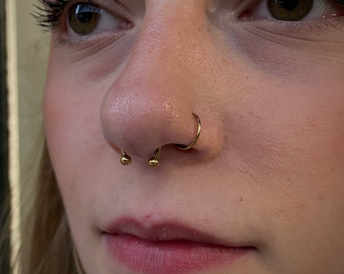 Thick gold circular barbell septum piercing on a person's nose.