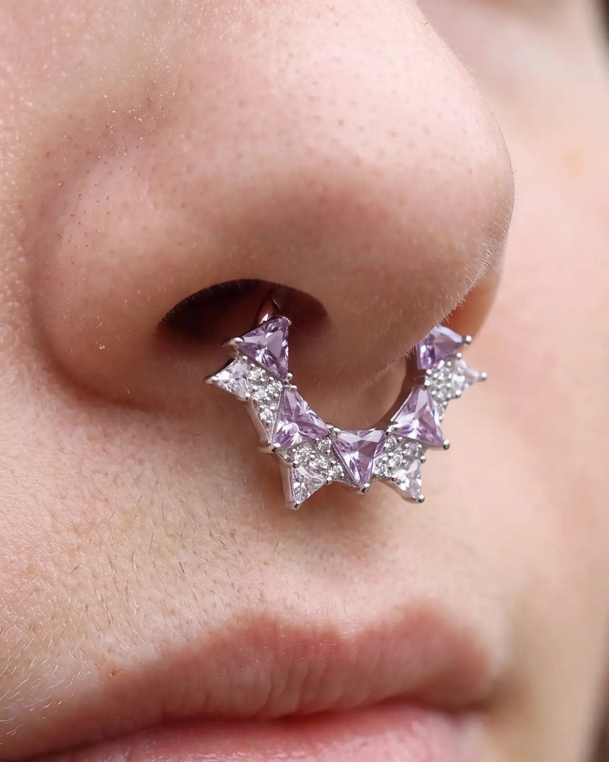 Thick silver septum piercing with purple triangular gemstones and small clear diamonds.