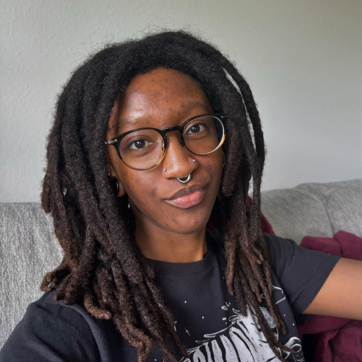 Person with dreadlocks and glasses wearing a thick silver septum hoop piercing.
