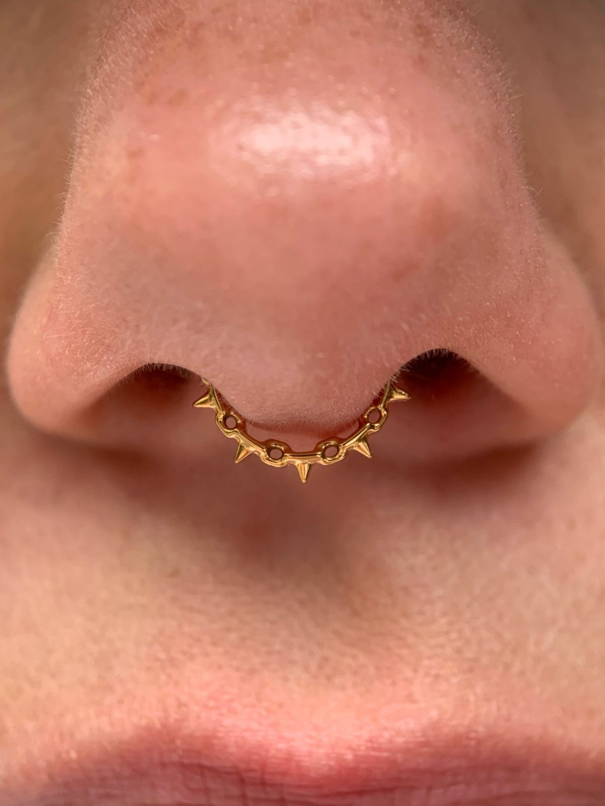 Gold-colored spiked septum ring piercing the nasal septum of a person.