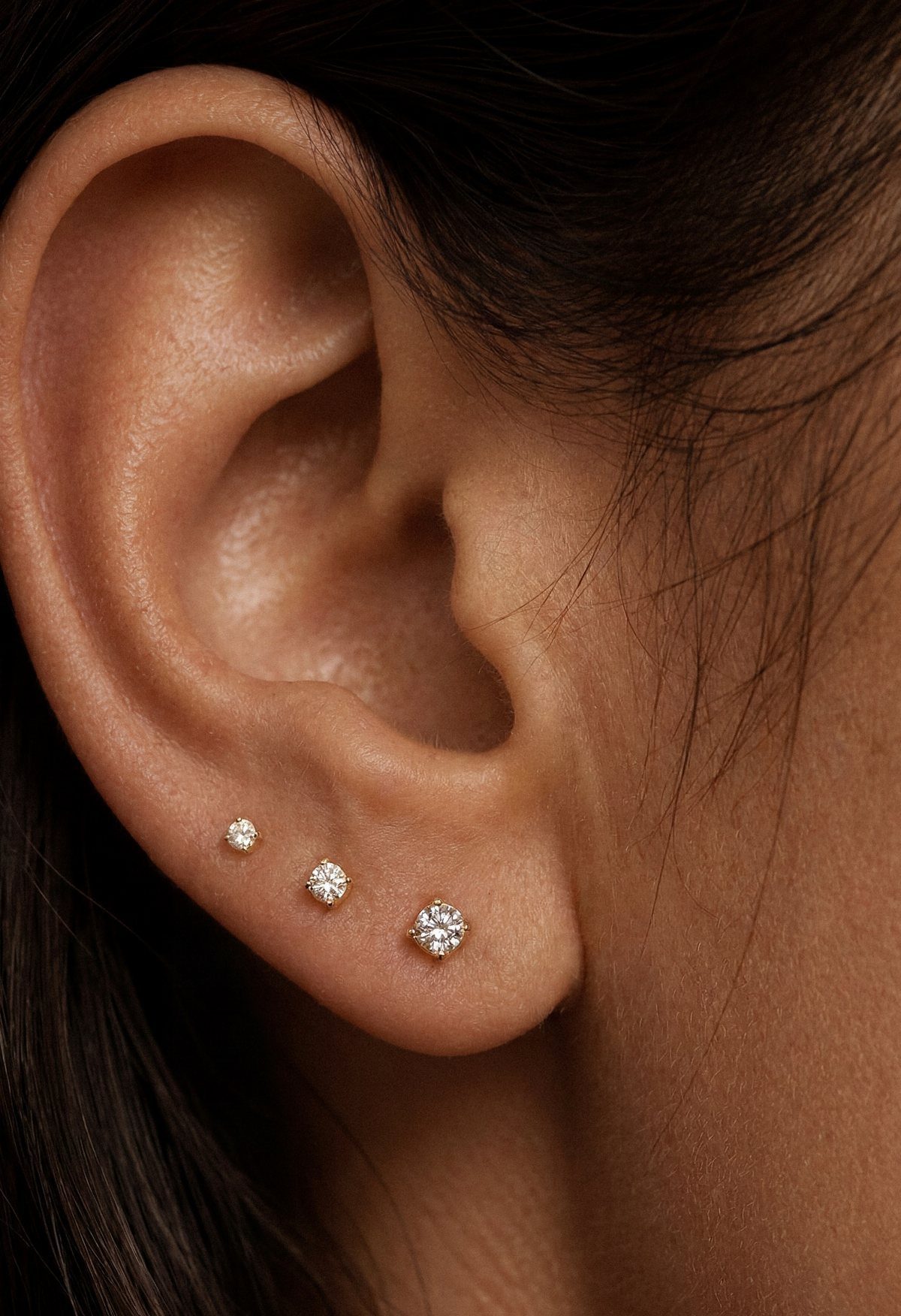 Three silver diamond stud earrings of different sizes in a linear lobe piercing.
