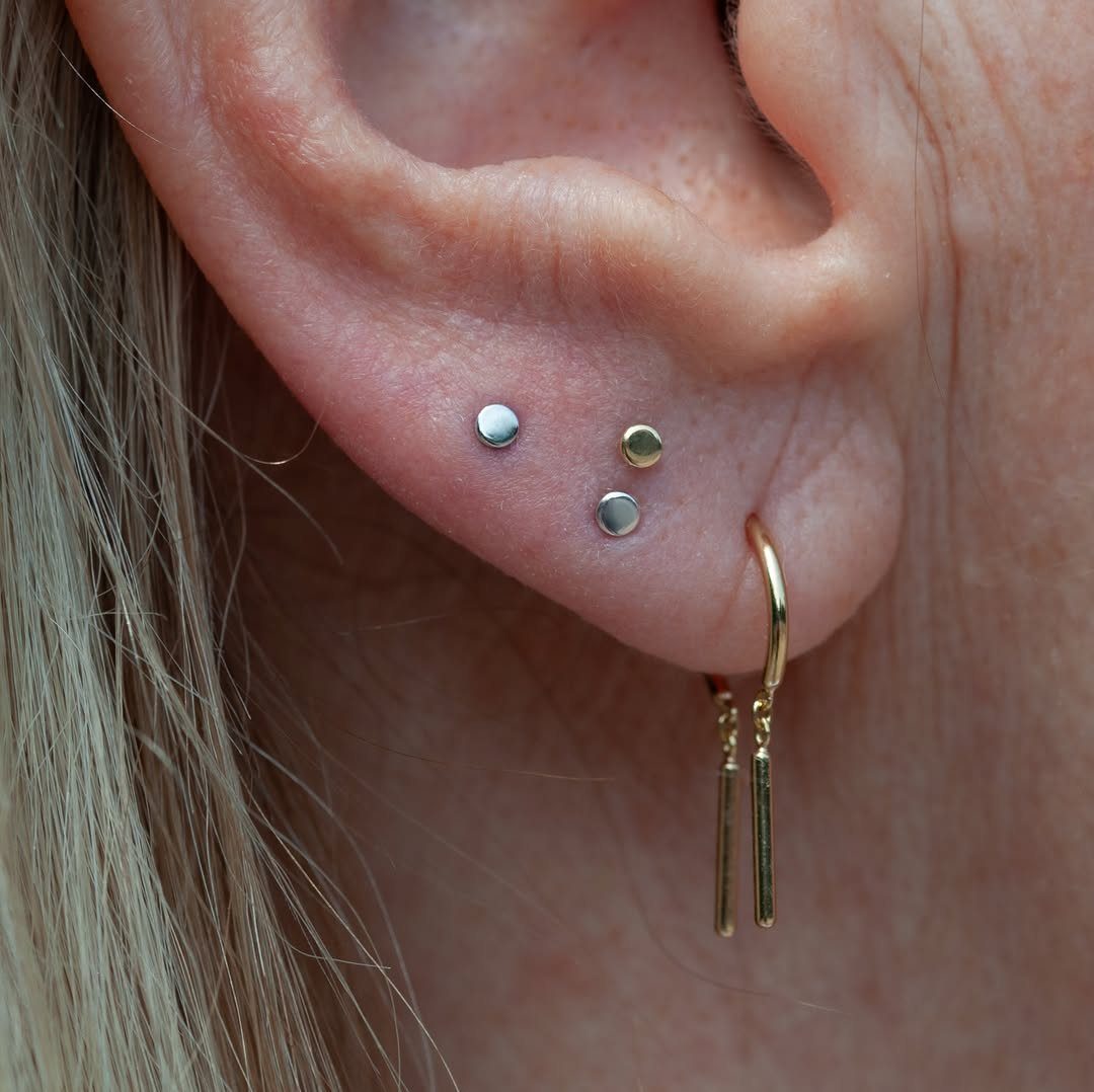 Human earlobe with a gold hoop and mixed gold and silver stud piercings.