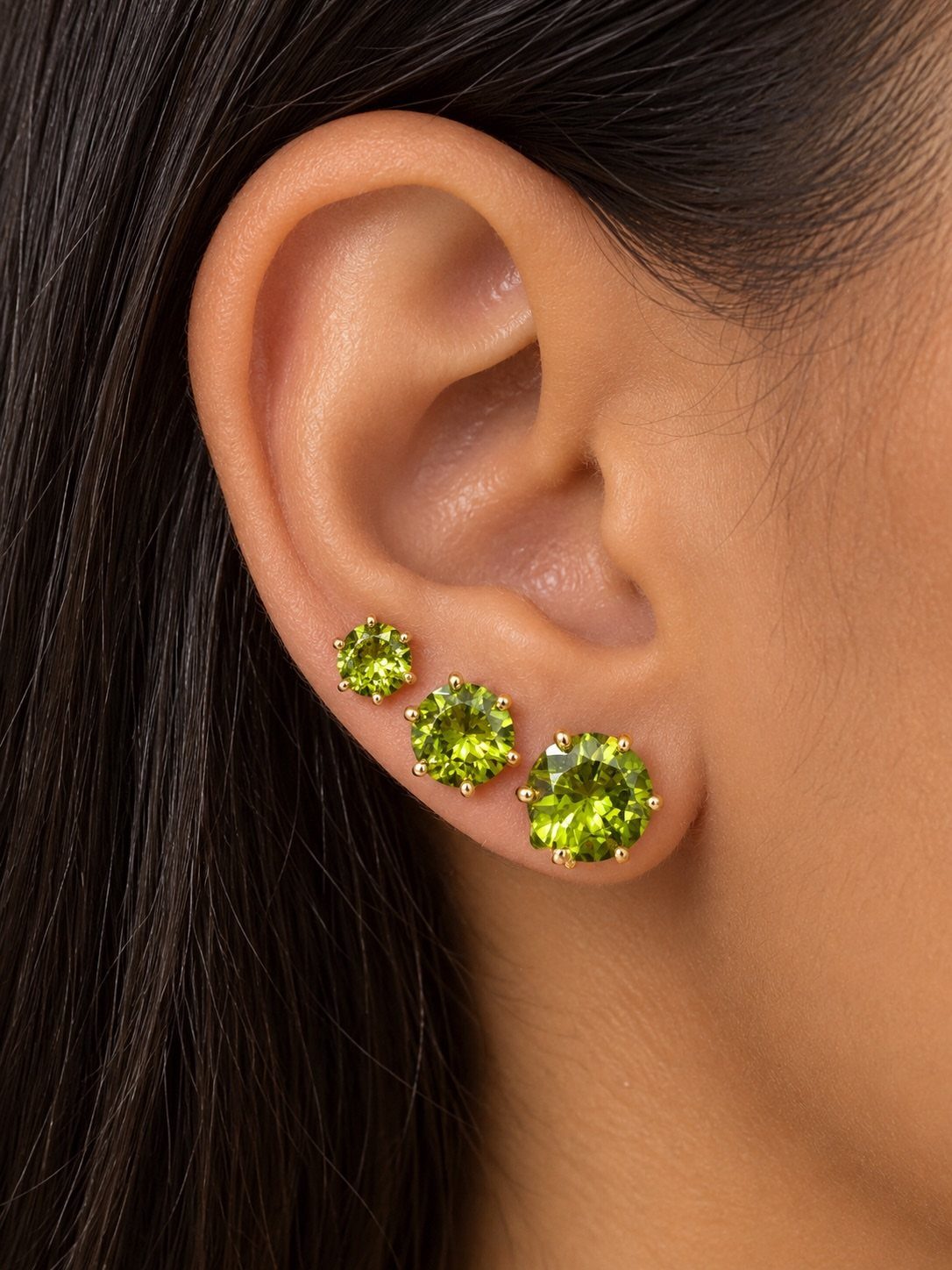 Three gold stud earrings with green gemstones in a triple lobe piercing sequence.