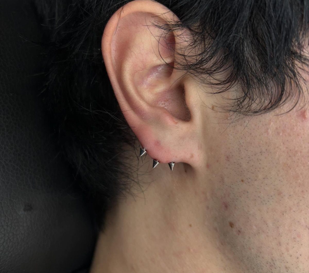 Ear lobe with three silver cone-shaped stud piercings in a horizontal row.