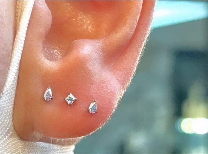 Human earlobe with three silver crystal stud piercings in a triple lobe arrangement.