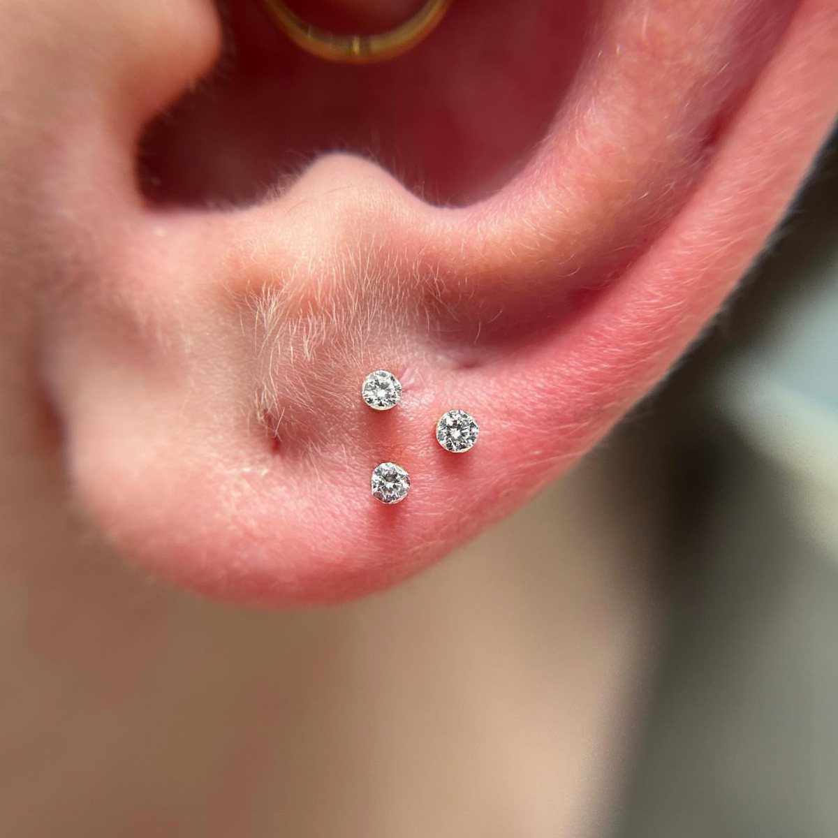 Three clear diamond stud earrings arranged in a triangular pattern on an earlobe.