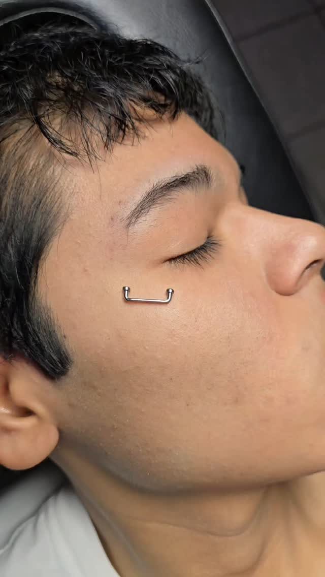 Silver barbell piercing on the upper cheekbone of a person's face.