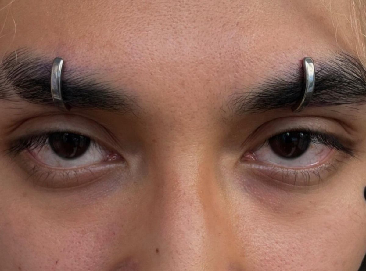 Person with silver curved barbell piercings in both of their eyebrows.