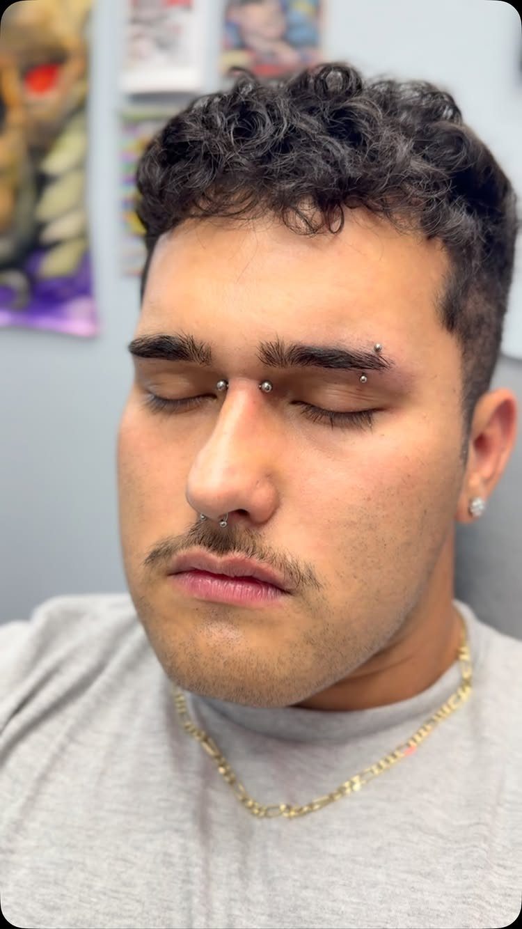 Man with a bridge piercing on his nose and an eyebrow piercing.