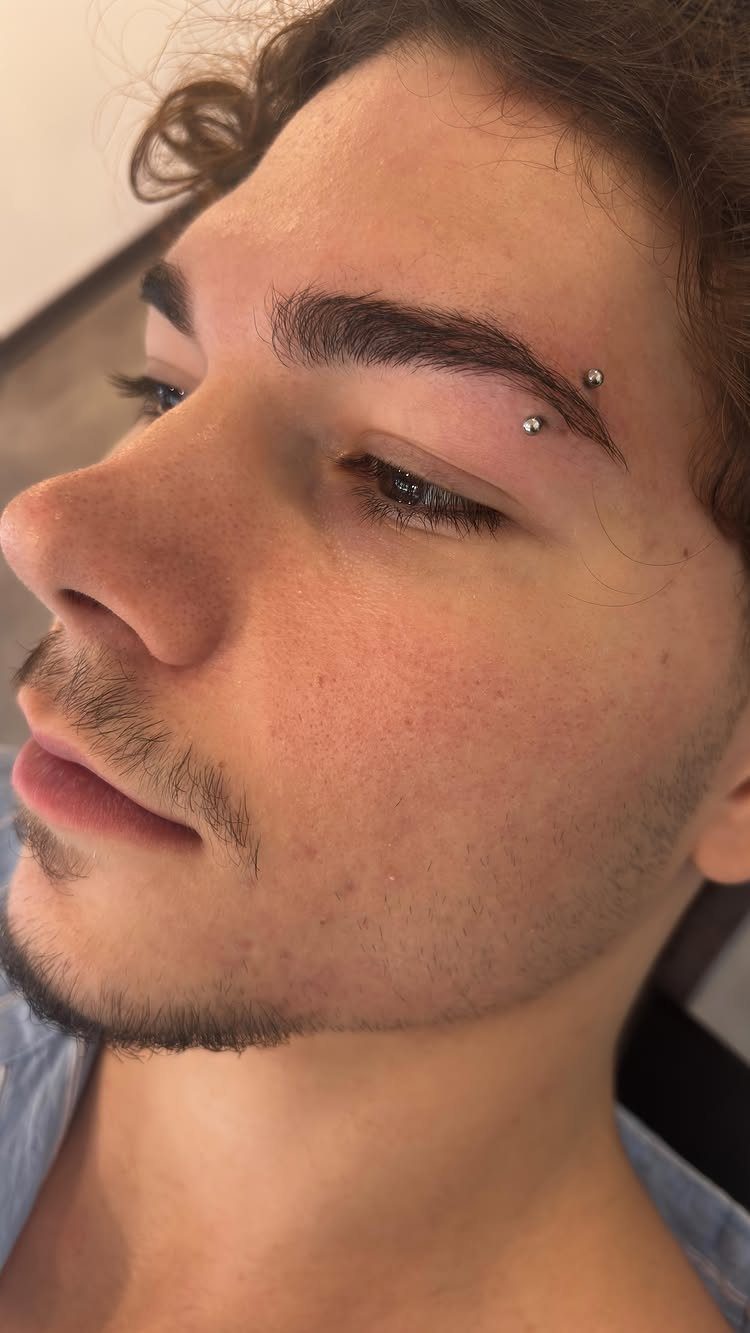 Person with a vertical eyebrow piercing featuring silver beads on the brow arch.