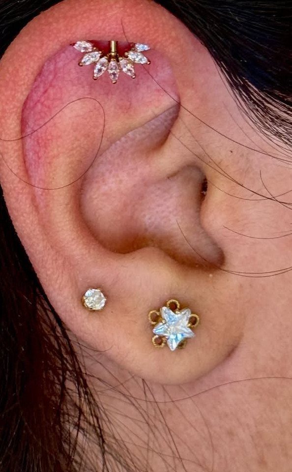 9 Upper Cartilage Piercing Ideas, Jewelry, and Aftercare 7 Ear with a gold fan-shaped upper cartilage piercing and lobe jewelry.
