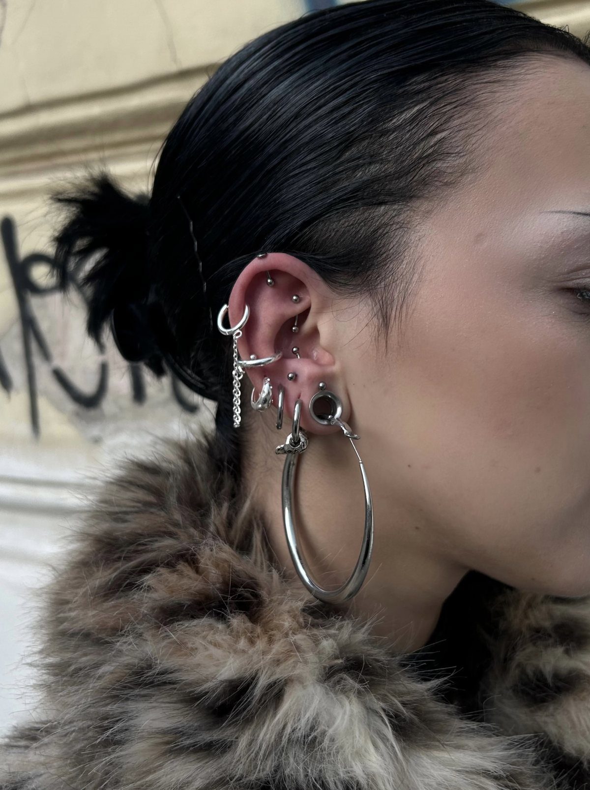 9 Upper Cartilage Piercing Ideas, Jewelry, and Aftercare 2 Ear with multiple silver piercings including upper cartilage studs and a large hoop earring.
