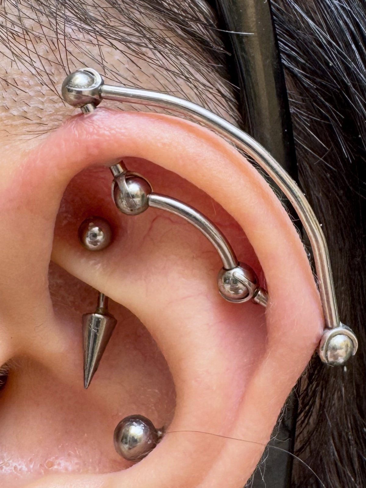9 Upper Cartilage Piercing Ideas, Jewelry, and Aftercare 3 Human ear featuring an industrial piercing with a long silver barbell across the top.
