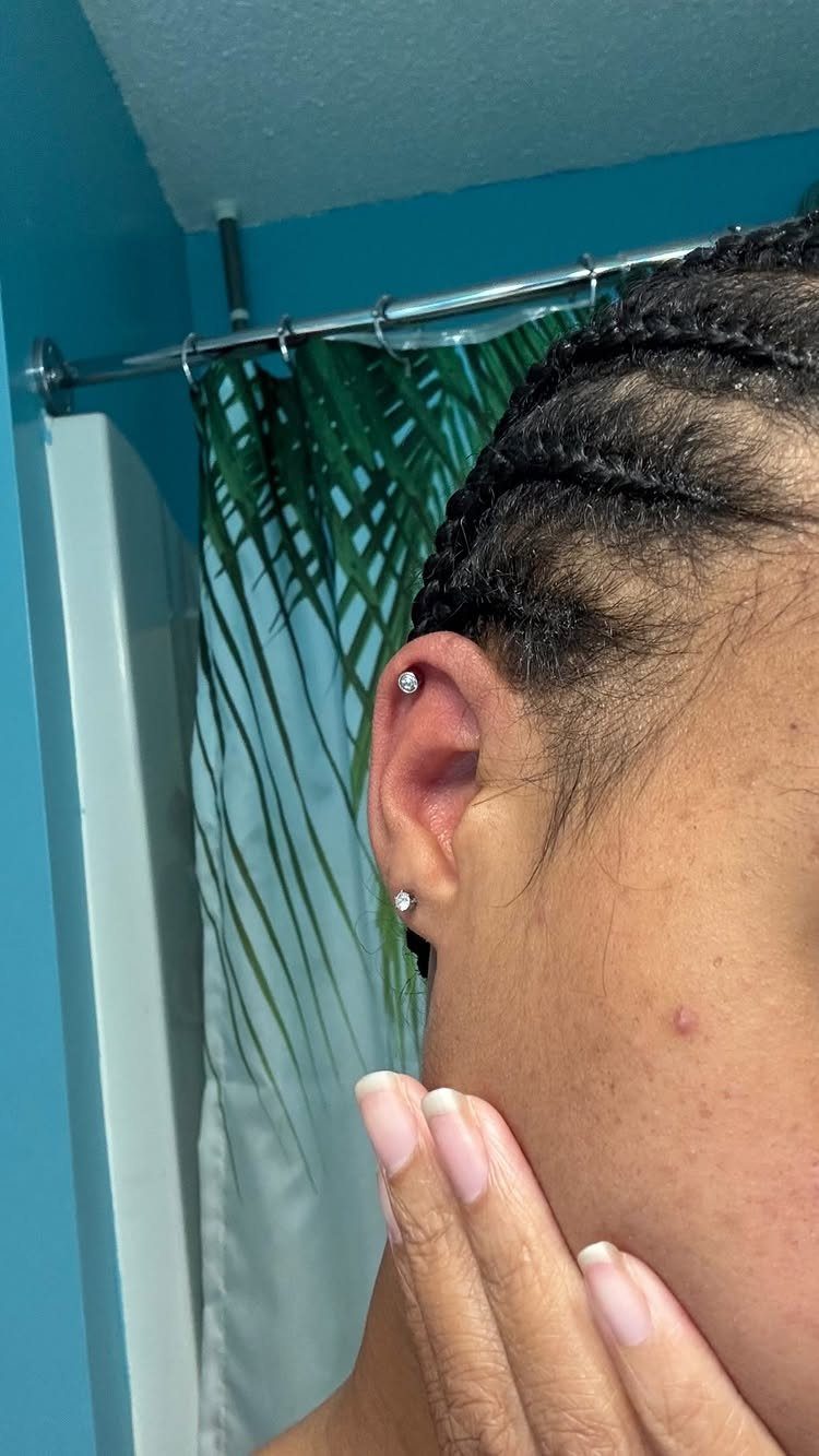 9 Upper Cartilage Piercing Ideas, Jewelry, and Aftercare 9 Ear with braided hair featuring a silver stud in the upper cartilage piercing.