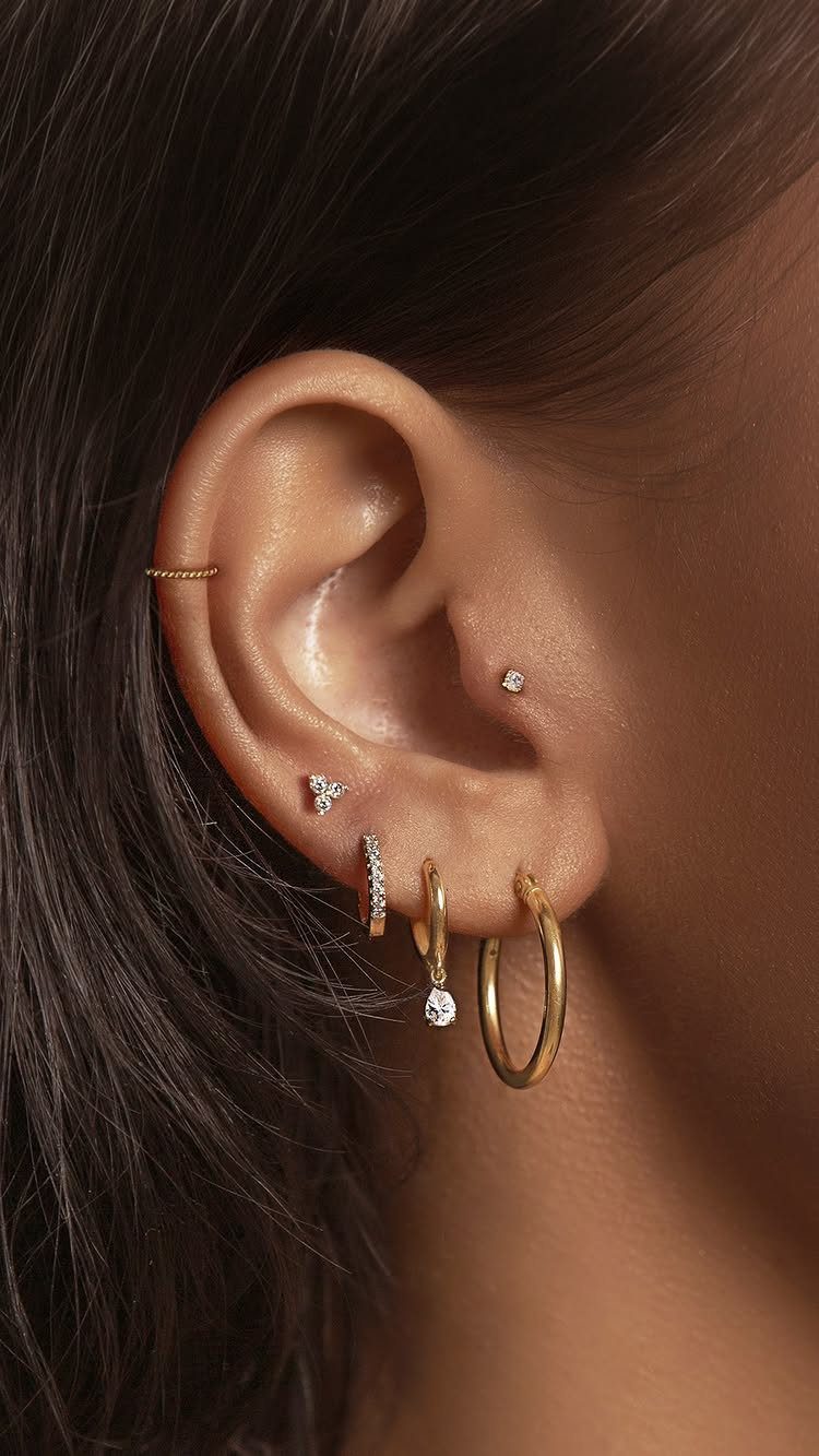 9 Upper Cartilage Piercing Ideas, Jewelry, and Aftercare 1 Ear with gold studs and hoops, including a small hoop in the upper cartilage.
