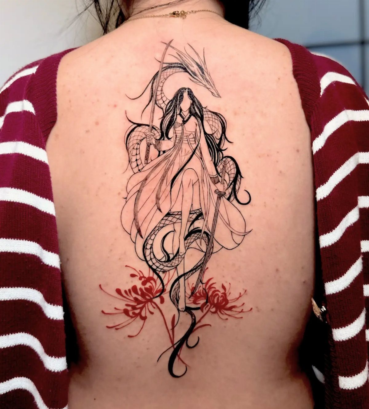 Female warrior and dragon tattoo with red flowers on a woman's back