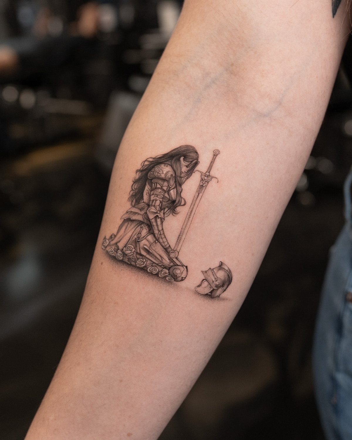 Female warrior tattoo on a forearm showing a kneeling knight with a sword.