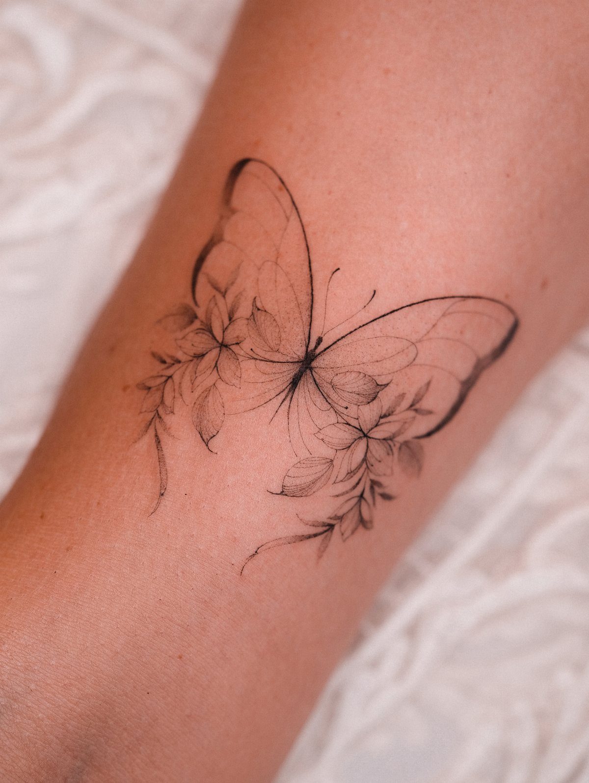 Butterfly tattoo with floral elements on a person's arm in black ink