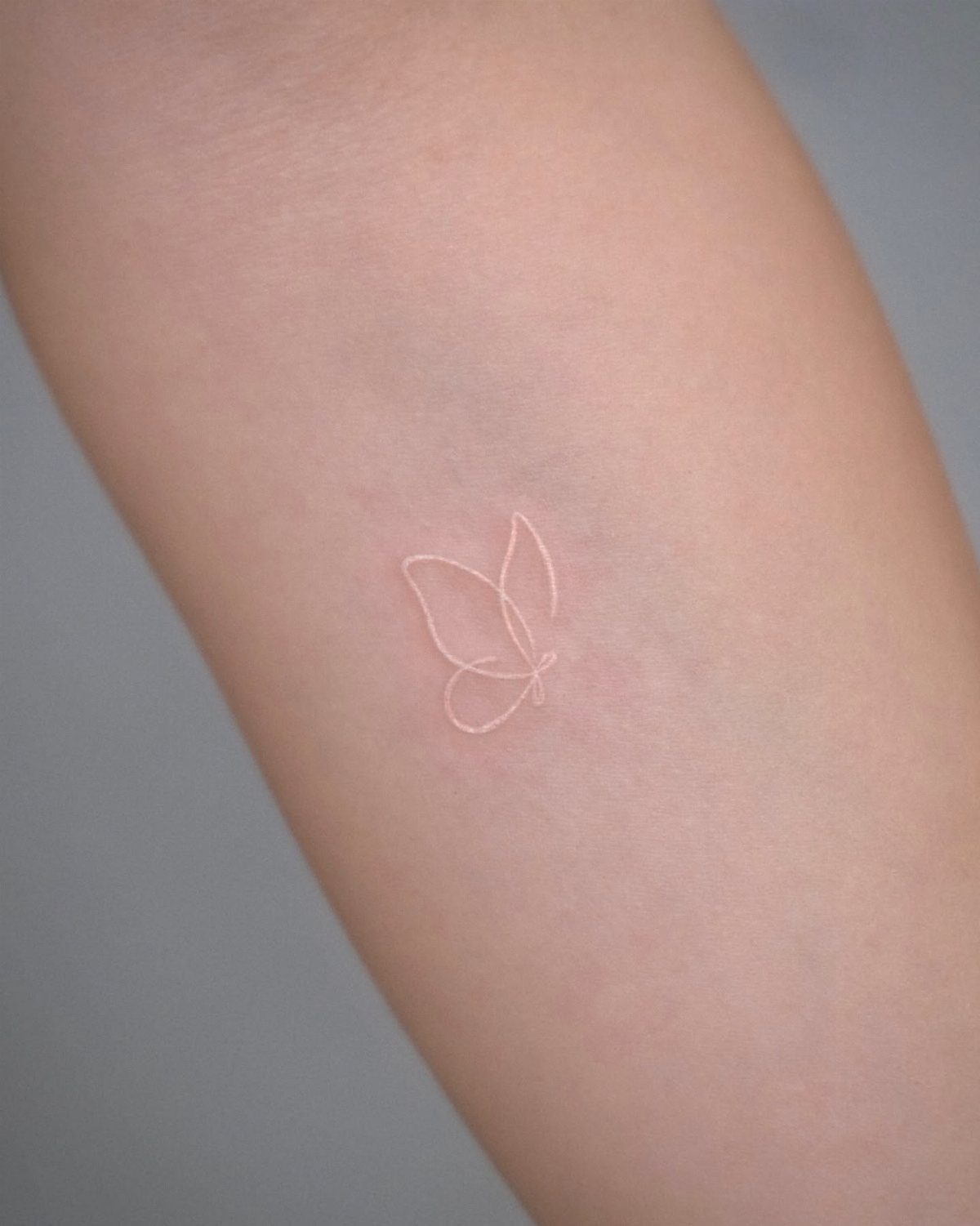 Small white ink butterfly tattoo outline on a person's pale forearm.